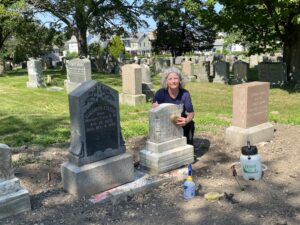 A woman squats next to headstone and cleans it with a scrub brush
