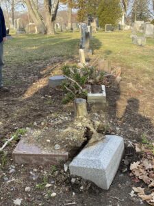 Fallen headstones with a cut down brush disturbing their base